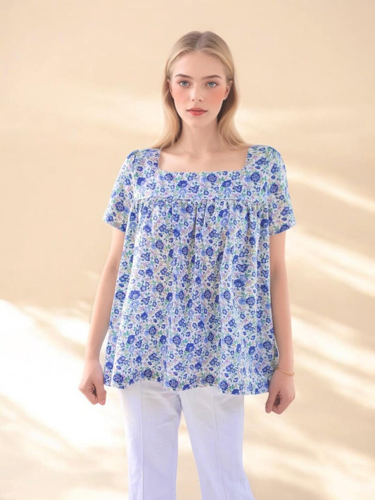May include: A square-neck top with short sleeves, featuring a blue floral pattern on a white background. The top is paired with white pants. The overall style is casual and feminine, suitable for warm weather.